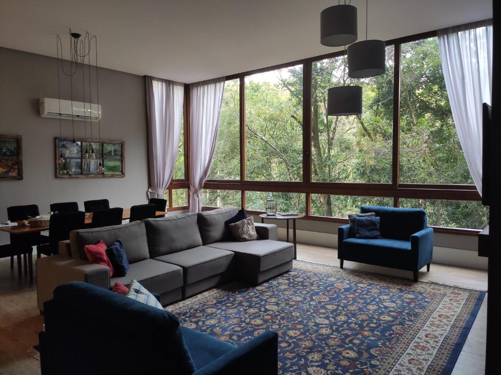 uma sala de estar com um sofá, cadeiras e janelas em GRAMADO MINHA CASA Apartamento Premium - Centro em Gramado