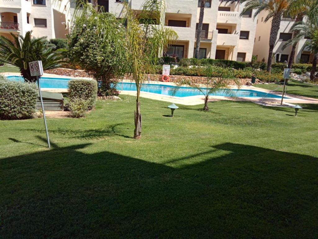 un pequeño árbol en el césped cerca de una piscina en Bevs ground floor Roda Golf Apartment!, en San Javier