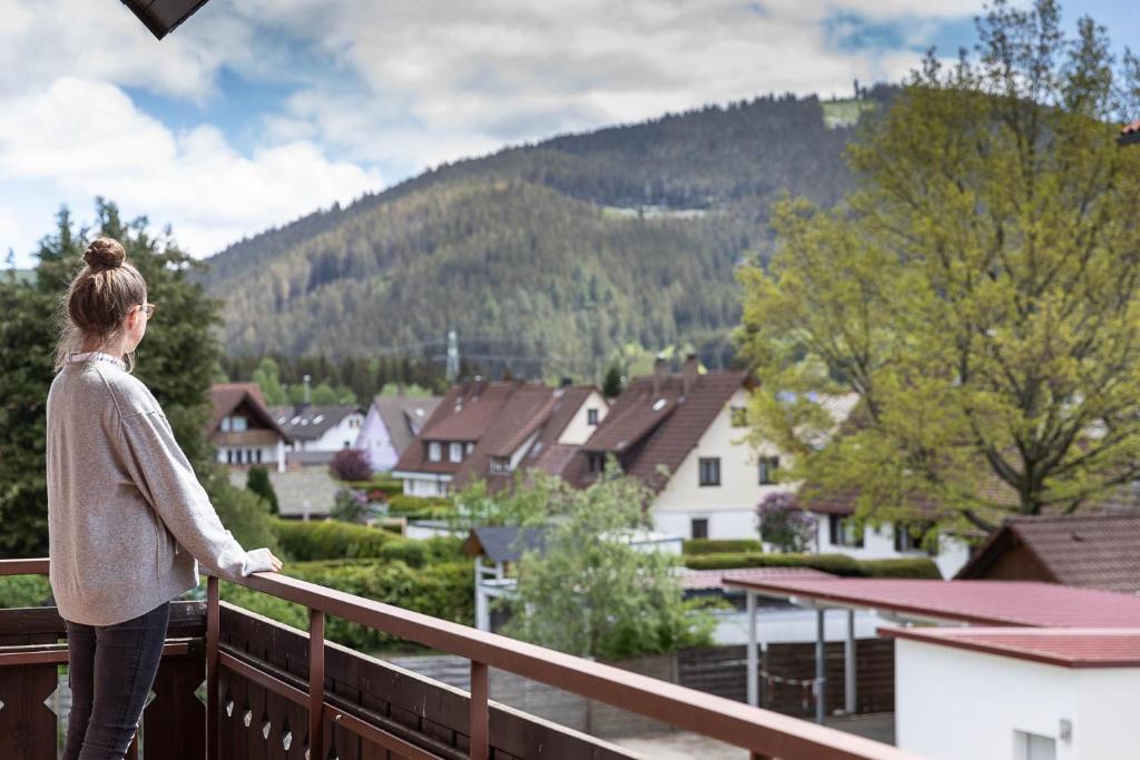 a woman standing on a balcony looking out at a town at WÄLDER: Quartier Titisee in Titisee-Neustadt