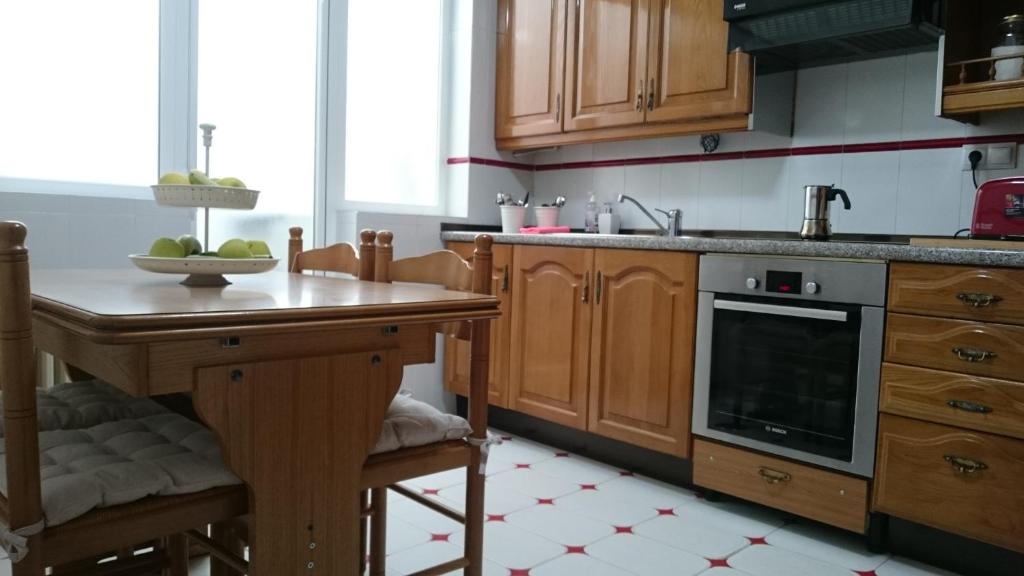una cocina con armarios de madera y una mesa con un bol de fruta en Casa de Huéspedes Vecinodecerbantes, en Alcalá de Henares