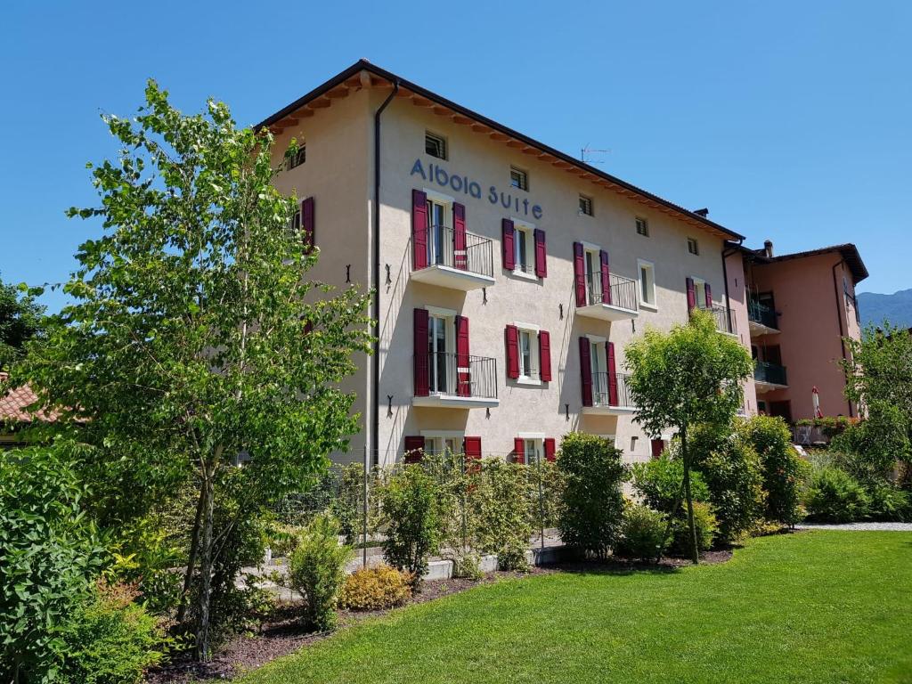 a building with red shuttered windows and a lawn at Albola Suite Holiday Apartments in Riva del Garda
