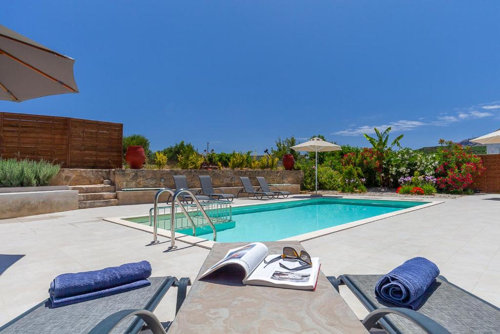a swimming pool with chairs and a book on a table at Trialonia Luxury Villa in Kissamos