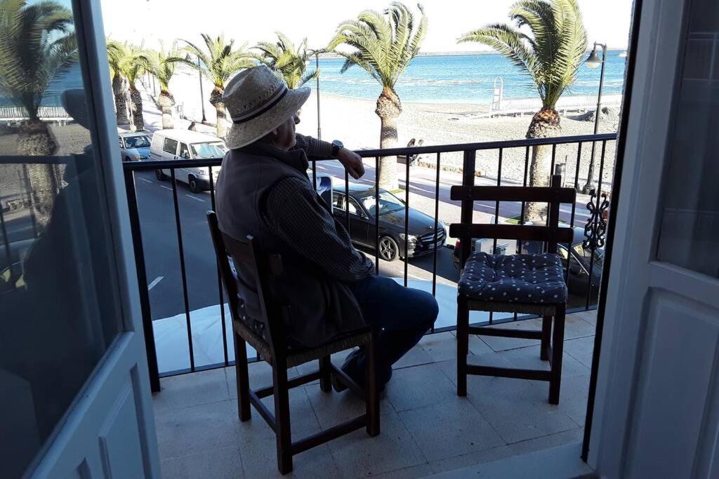 un hombre sentado en una silla en un balcón con vistas a la playa en Piso en primera línea con wifi y vistas al mar, en Lo Pagán