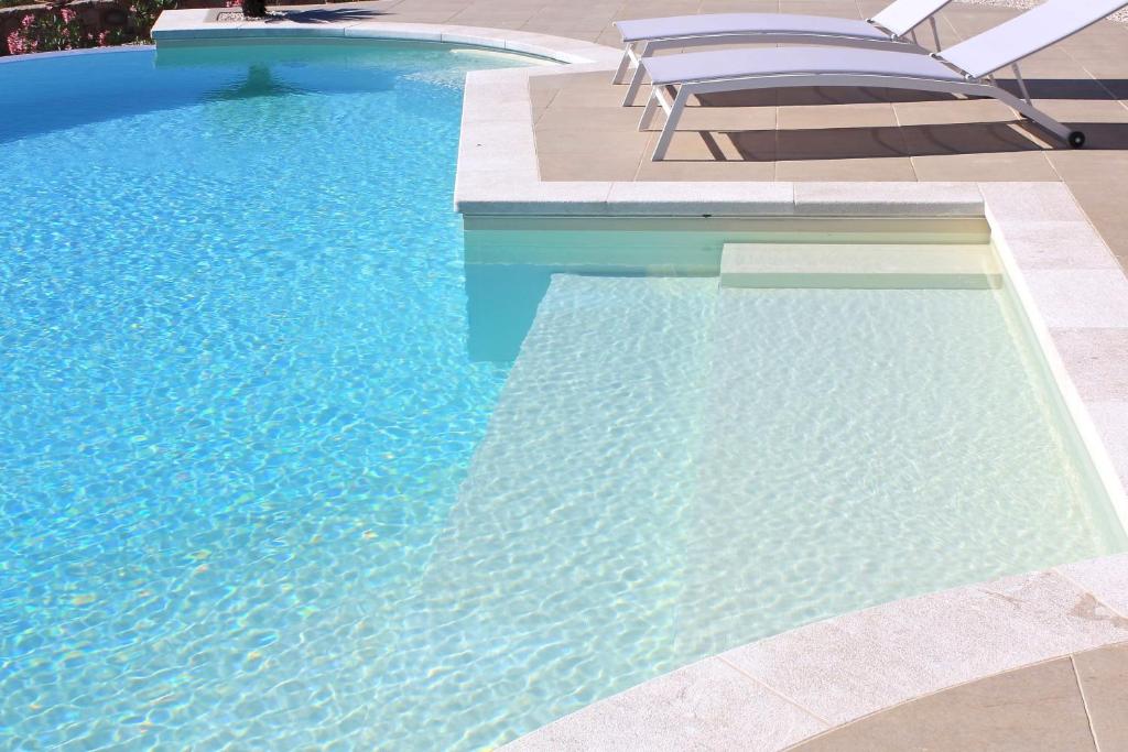 une piscine avec de l'eau bleue et des chaises dedans dans l'établissement VILLA ALBA NUOVA with infinity pool & amazing sea view, à Golfo Aranci