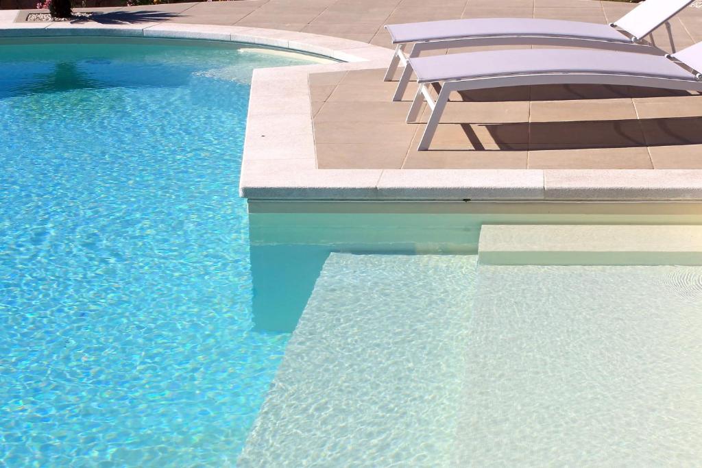 - une piscine avec des chaises et de l'eau bleue dans l'établissement VILLA ALBA NUOVA with infinity pool & amazing sea view, à Golfo Aranci