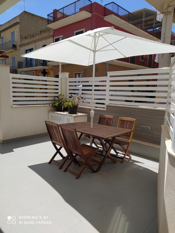 una mesa de madera y sillas con una sombrilla en el balcón en Iris, en Marina di Ragusa
