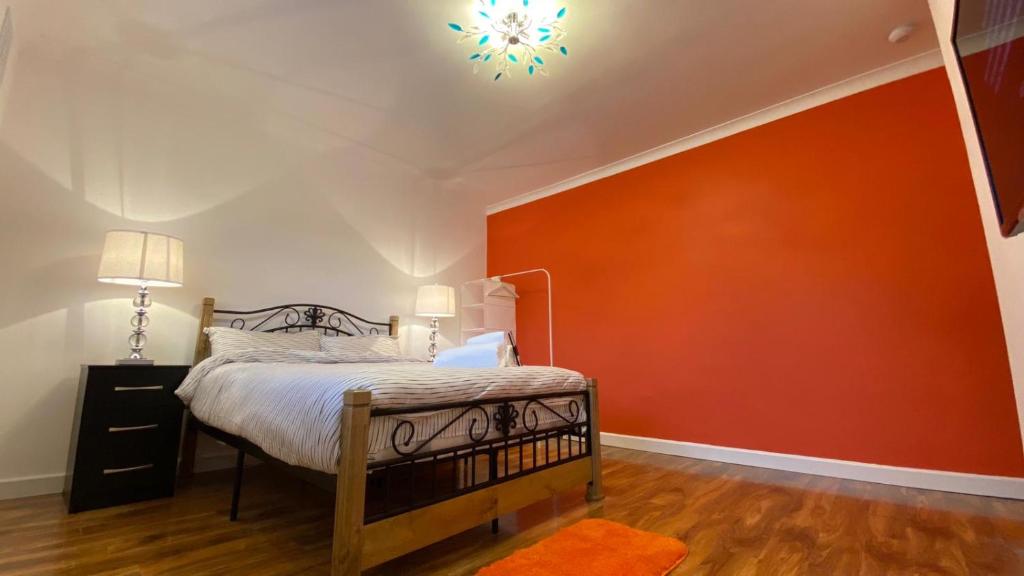 Schlafzimmer mit einem Bett mit orangefarbener Wand in der Unterkunft Grand Heights LUXURY Suites in London