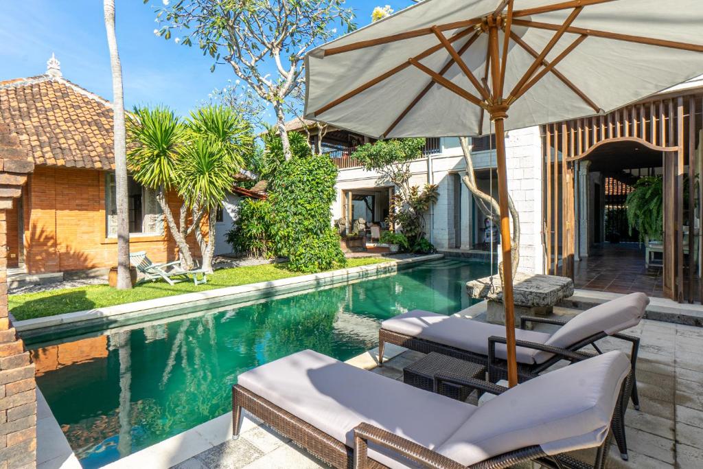 a pool with chairs and an umbrella next to a house at Villa Angsa by Nakula in Sanur