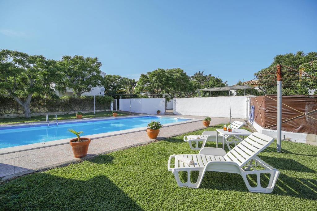 Un patio con dos sillas blancas y una piscina. en Los paraisos 1, en Conil de la Frontera