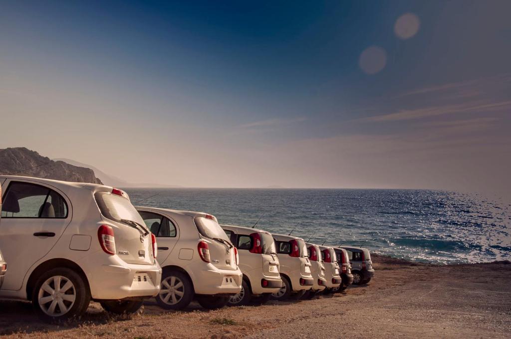 a row of white cars parked next to the ocean at Alpha Studios in Arkasa