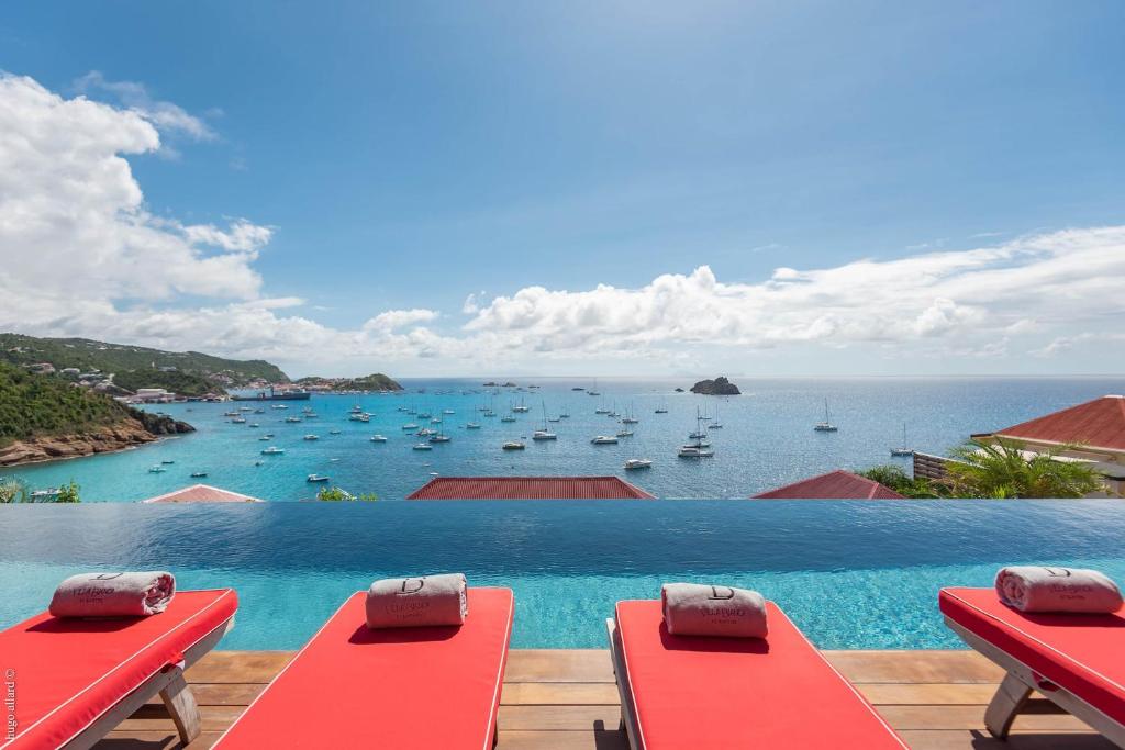 a pool with red benches and a view of the ocean at Dream Villa Corossol 706 in Saint Barthelemy