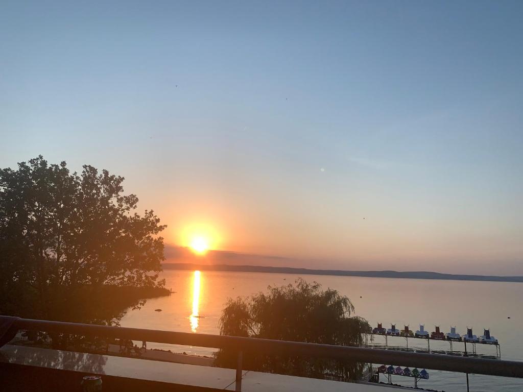 einen Sonnenuntergang über dem Wasser mit Leuten auf einem Pier in der Unterkunft Lakeside Wellness Apartman in Siófok