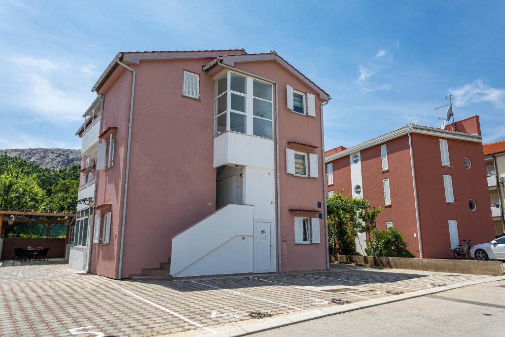 a red building with a white door next to a brick building at Apartments La Natalli in Baška