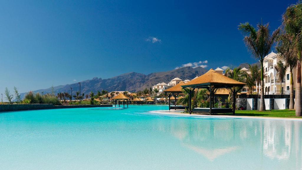 a beach with palm trees and a pool of water at Gran Melia Palacio de Isora Resort & Spa in Alcalá
