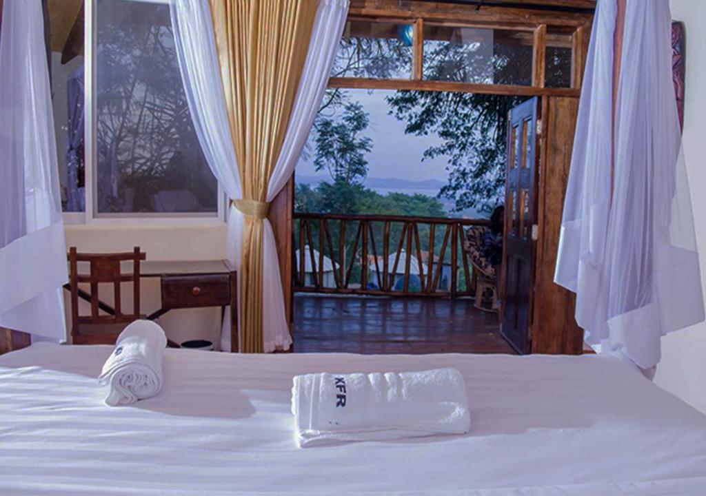 a bed with a towel on it with a balcony at Kampala Forest Resort - KFR Lodge in Kampala