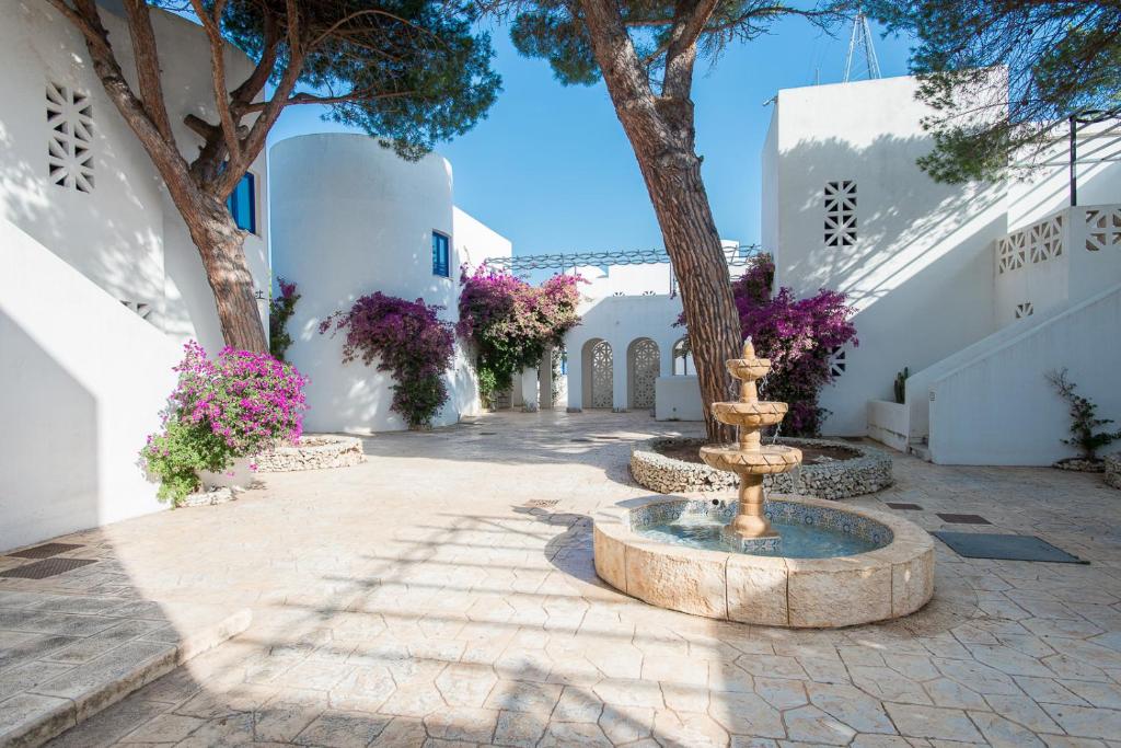 a courtyard with a fountain and trees and white buildings at Araba Fenice Village in Torre dell'Orso