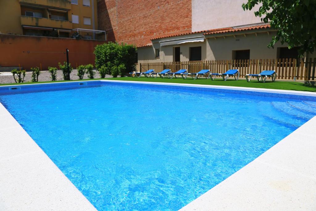 a blue swimming pool with chairs and a building at RVHotels Apartamentos Provenzal in L'Escala