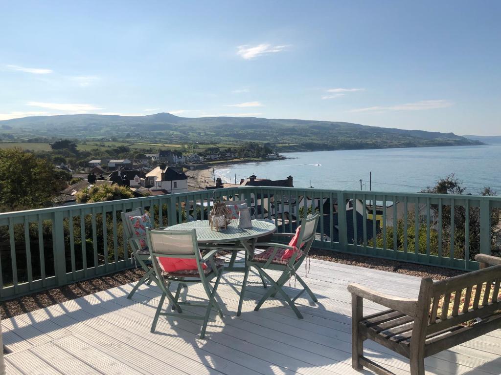 a table and chairs on a deck with a view of the water at Ballygally Seaview Cottage in Larne