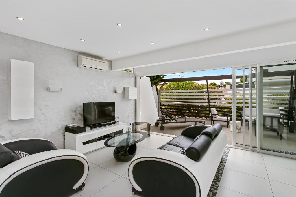 d'un salon avec canapés et télévision ainsi que d'un balcon. dans l'établissement Village Naturiste - La Villa Tentation Port Nature Luxe, au Cap d'Agde