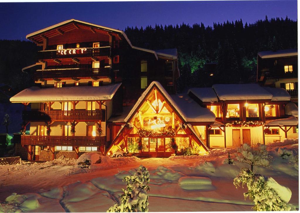 een groot houten huis met 's nachts sneeuw bij Hotel Club Le Crêt in Morzine