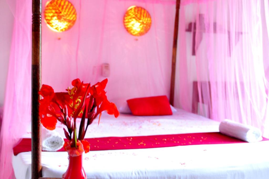 Cette chambre comprend un lit avec des fleurs rouges dans un vase. dans l'établissement Surewo Sun Shine Apartment, à Bentota