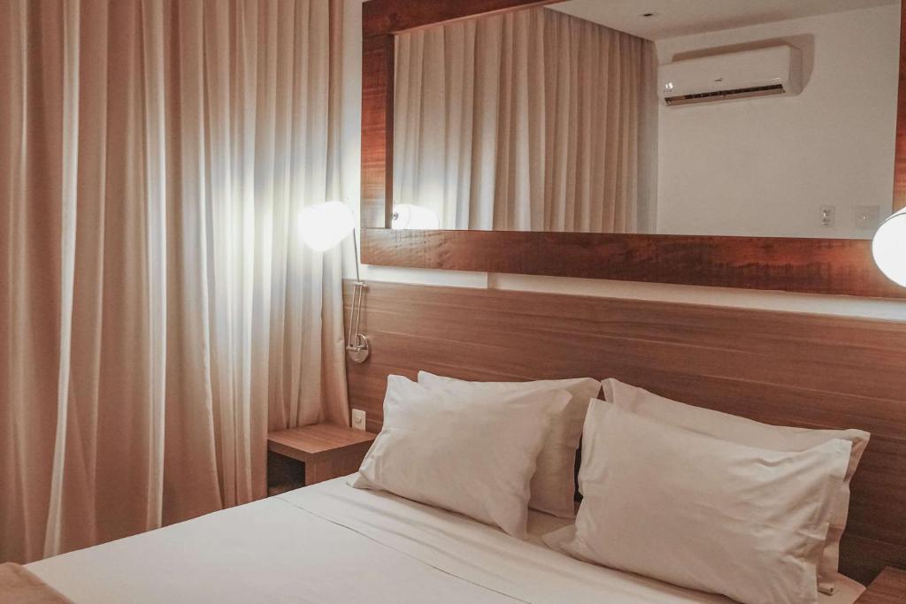 1 dormitorio con cama con almohadas blancas y espejo en Samba Rio Convention & Residence, en Río de Janeiro