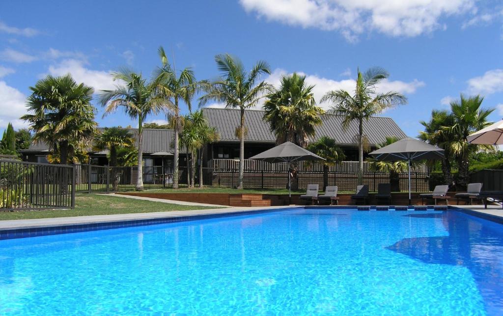 uma grande piscina azul com palmeiras e guarda-sóis em Kerikeri Homestead Motel & Apartments em Kerikeri