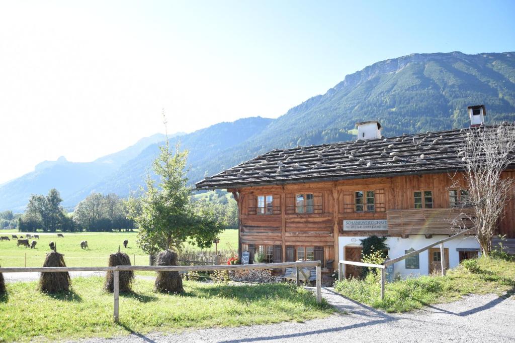 een houten huis in een veld met bergen op de achtergrond bij Ferienwohnung Schankwirtschaft Wohlfart in Pfronten