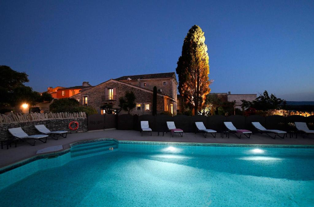 a swimming pool with chairs and a tree at night at Bastide des Demoiselles in Roussillon