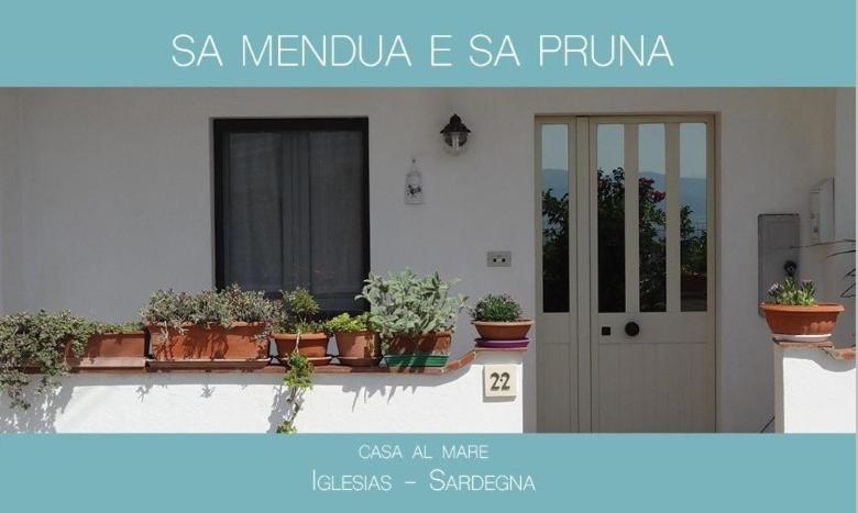 a white building with potted plants on a balcony at SA MENDUA E SA PRUNA casa al mare in Iglesias