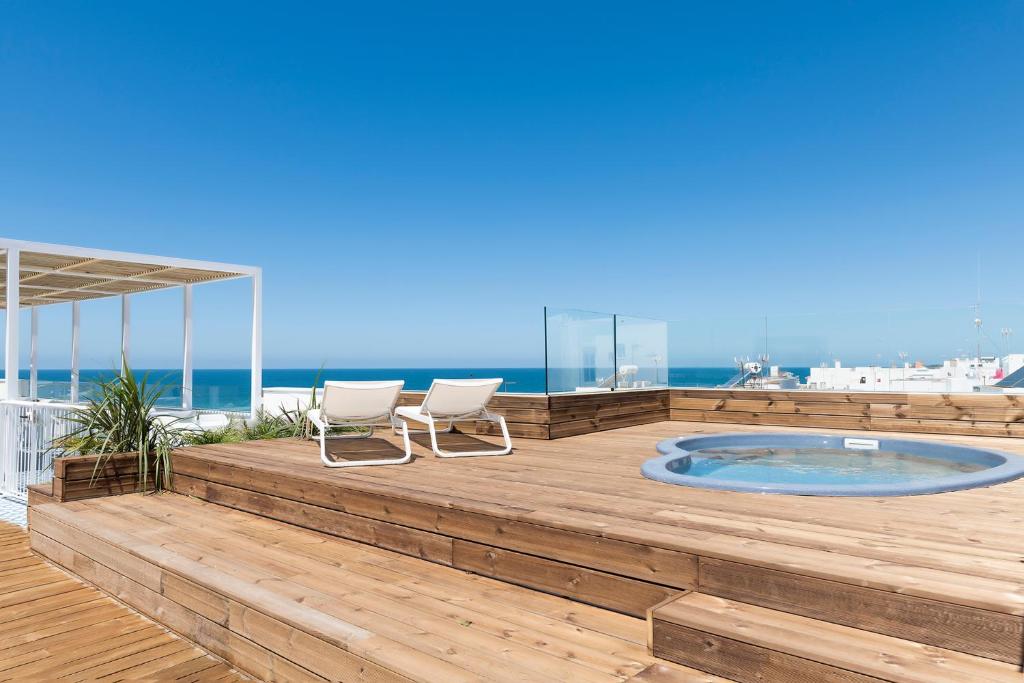 a deck with two chairs and a hot tub on the beach at Alzocaire Hostal Boutique in Conil de la Frontera