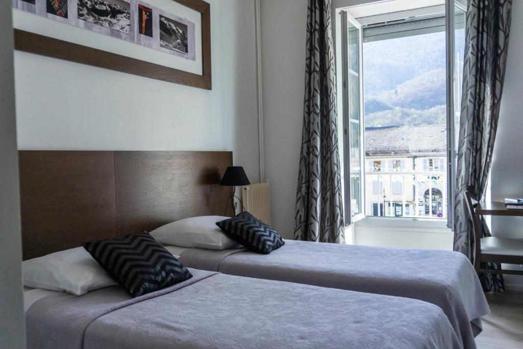 two beds in a hotel room with a window at Hôtel d'Ossau in Laruns