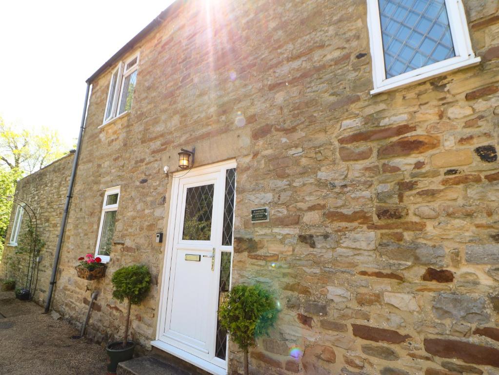 a stone house with a white door and windows at Bilberry Nook Cottage in Westgate