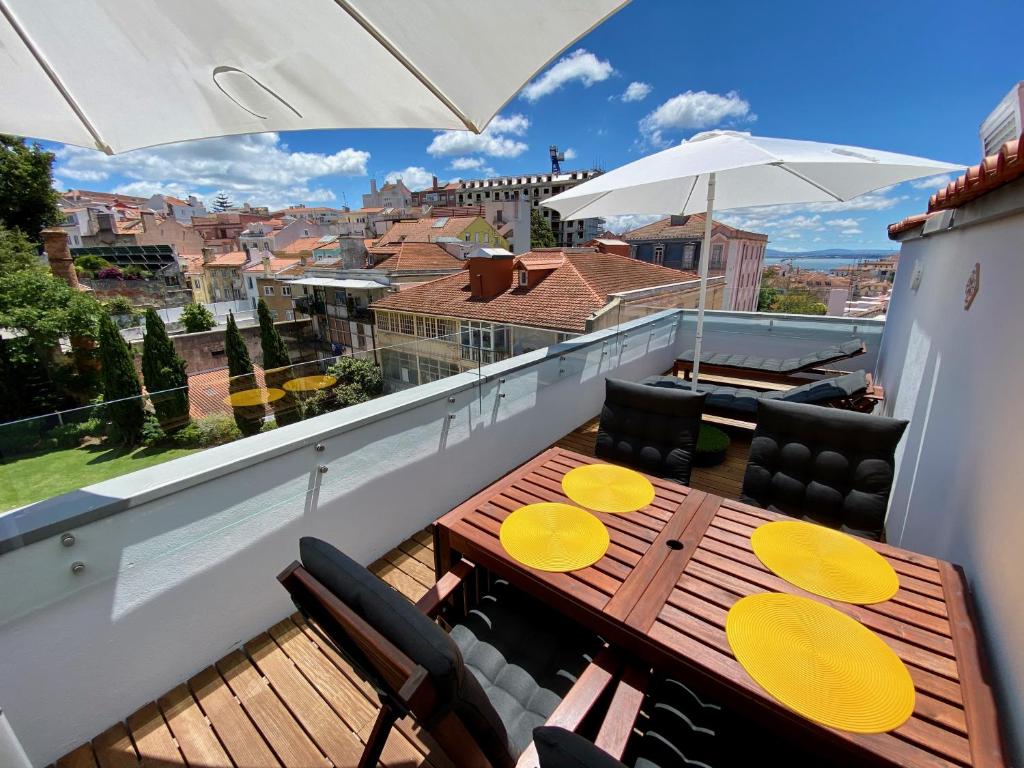 balcón con mesa de madera, sillas y sombrilla en Unique apartment by MyPlaceForYou, in the center of Lisbon with views over the city and the Tagus river en Lisboa