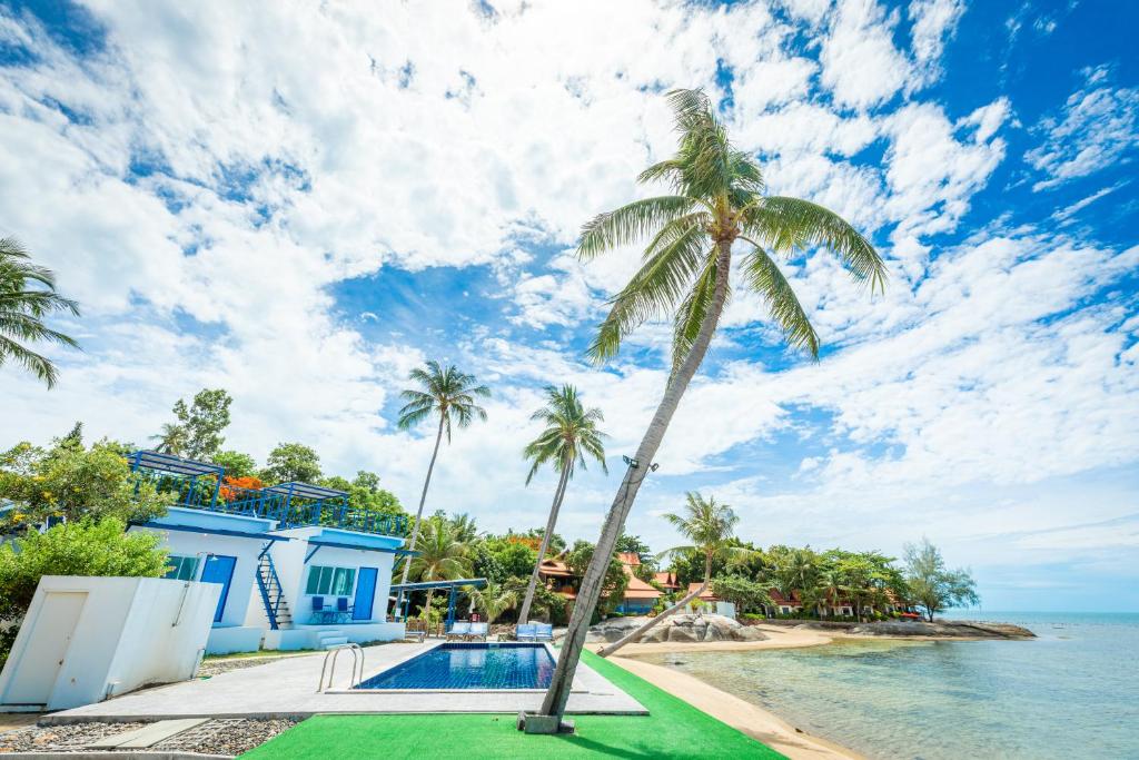 a palm tree next to a swimming pool next to the ocean at Three Trees Samui Resort - Sarocha Villa in Lamai