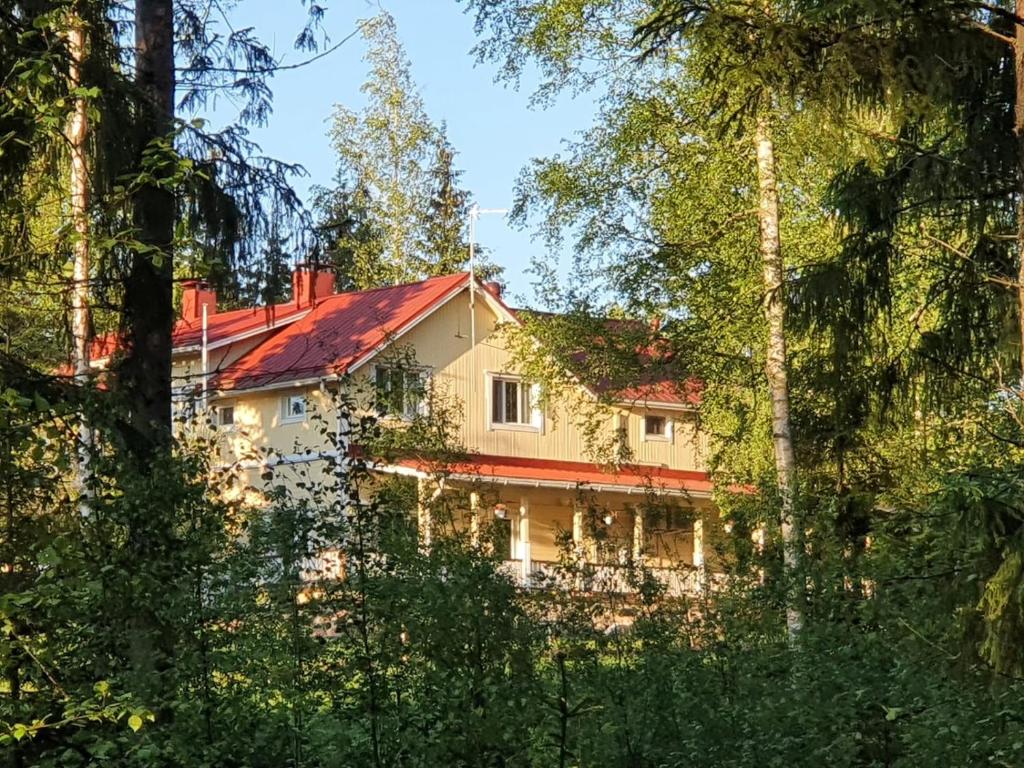uma casa com um telhado vermelho visto através das árvores em Tuhannen Tarinan Talo em Kannuskoski