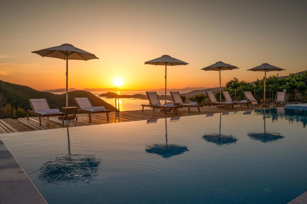 - une piscine avec des chaises et des parasols et le coucher du soleil dans l'établissement Ninemia Luxury Residence, à Perdika