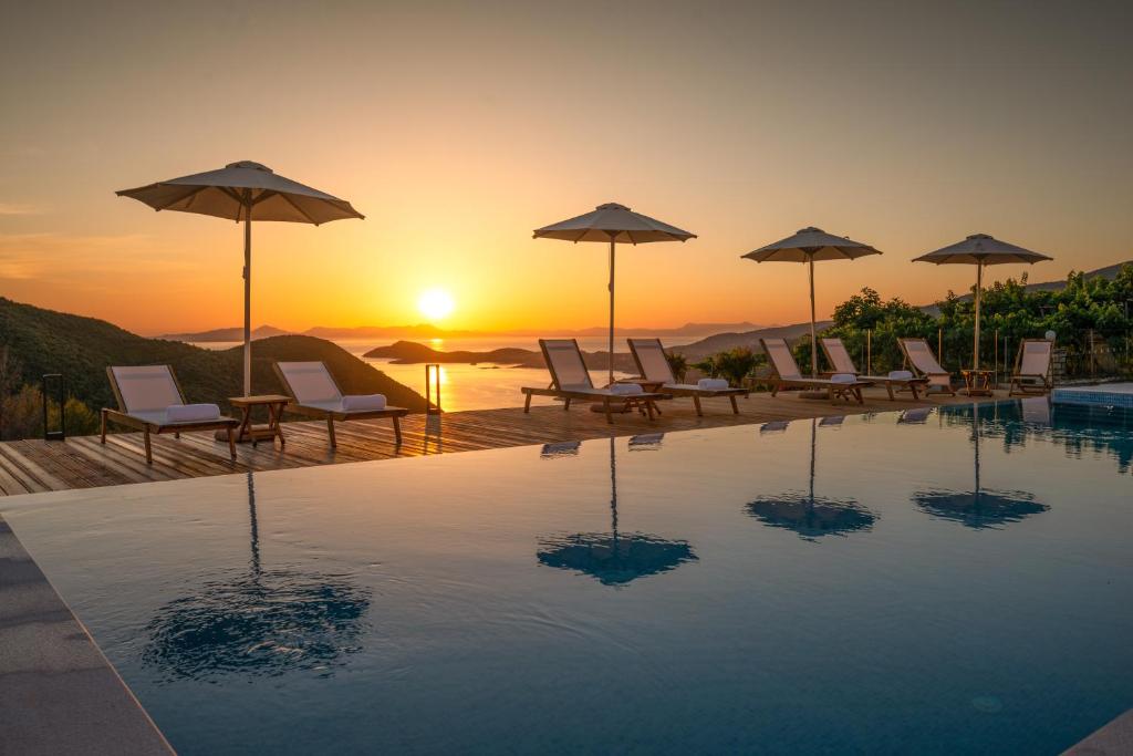 a pool with chairs and umbrellas and the sunset at Ninemia Luxury Residence in Perdika