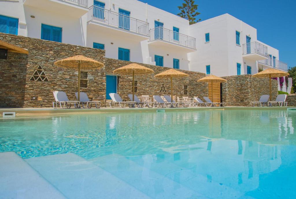 a swimming pool with chairs and umbrellas in front of a building at Ostria Hotel & Apartments in Gavrio