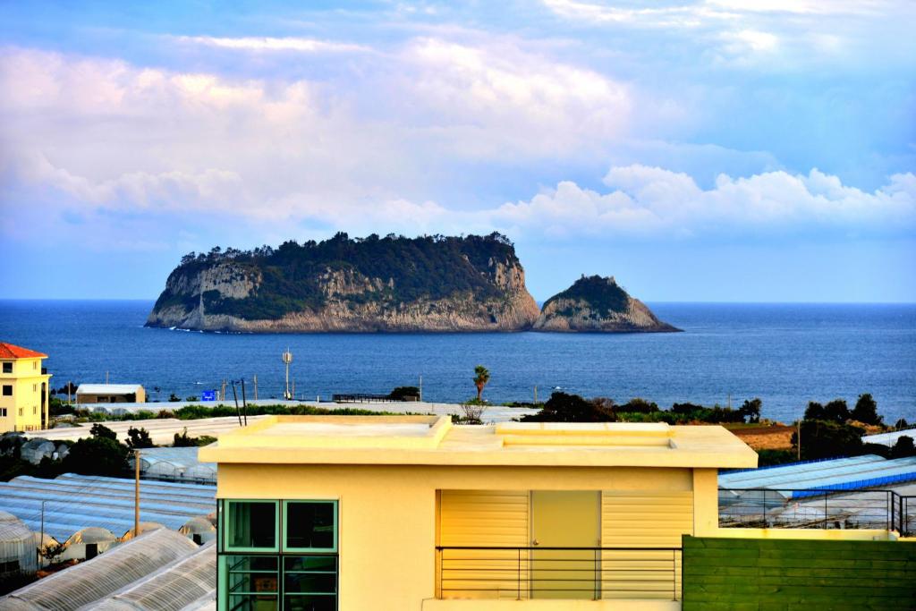 a yellow building with a view of an island in the ocean at Jeju Bada Wi Olle Pension in Seogwipo