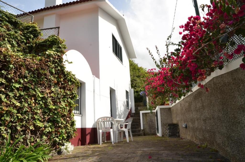 a white building with two chairs and pink flowers at Casinha do Paiol in Porto da Cruz