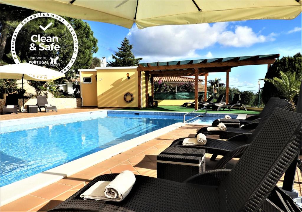 a pool with chairs and an umbrella next to a swimming pool at Hotel Rural Rocha da Gralheira in São Brás de Alportel