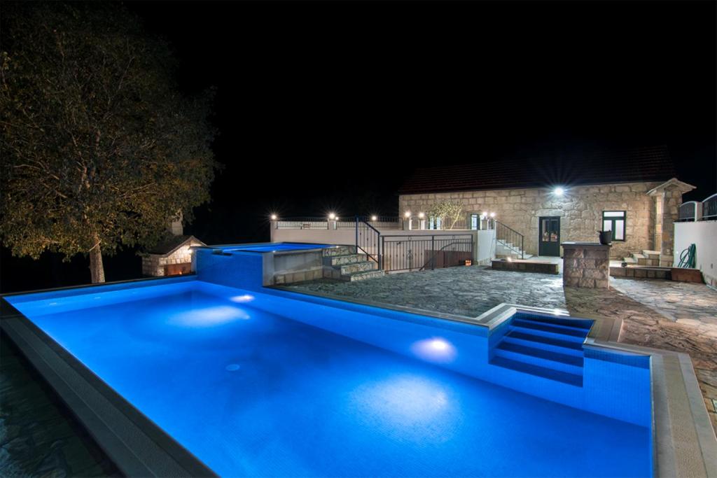 a large blue swimming pool in front of a house at night at Dvori Stipanovi with heated pool in Donje Rašćane