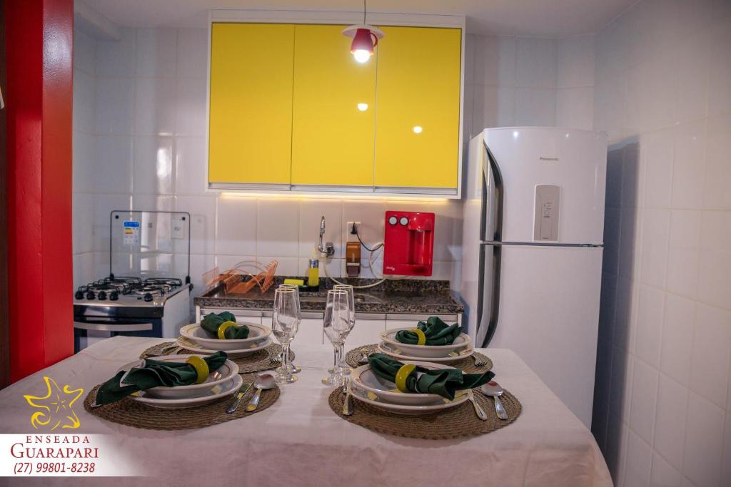 a kitchen with a table with plates and glasses and a refrigerator at MAIOR NOTA - 2 Quartos com AR CONDICIONADOS SPLIT, Air Fryer, Wi-Fi, Disney Plus, Star Plus, HBO Max, Guarda Sol, Cadeiras de Praia, Caixa Térmica, Churrasqueira, Rede para Descanso e Chuveirão - 8 pessoas - CONFORTO Máximo - Melhor Localização!! in Guarapari