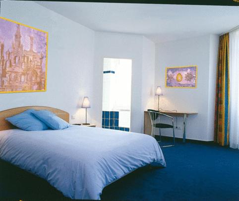 ein Schlafzimmer mit einem blauen Bett und einem Schreibtisch mit einem Computer in der Unterkunft Amadeus Hotel in Sarreguemines