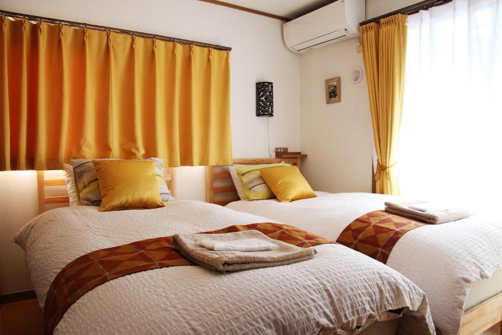 two beds in a room with yellow curtains at HAMA HILLS Shinjuku in Tokyo