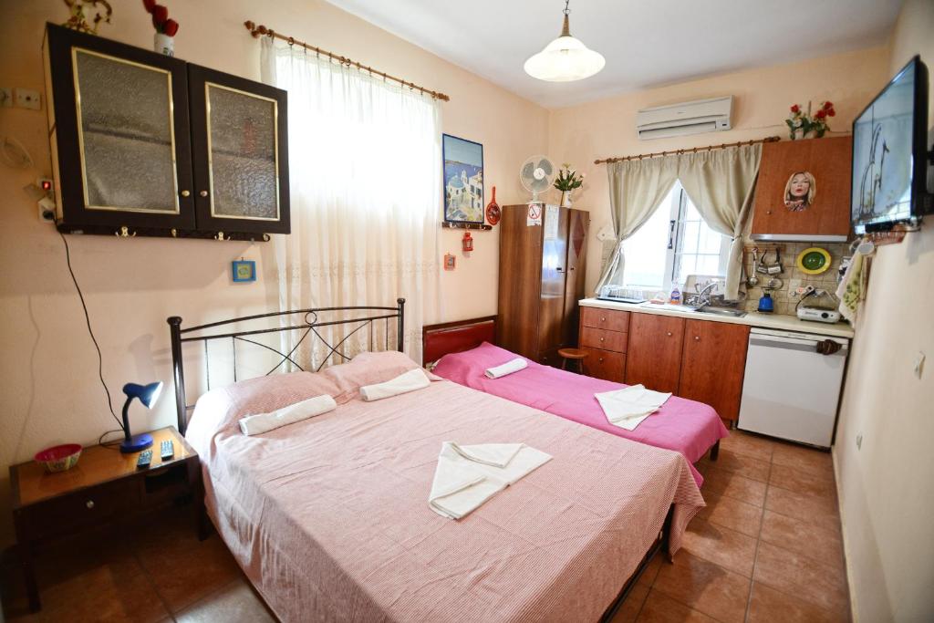 a bedroom with two beds with pink sheets and a kitchen at Ikaria Studios in Manganítis