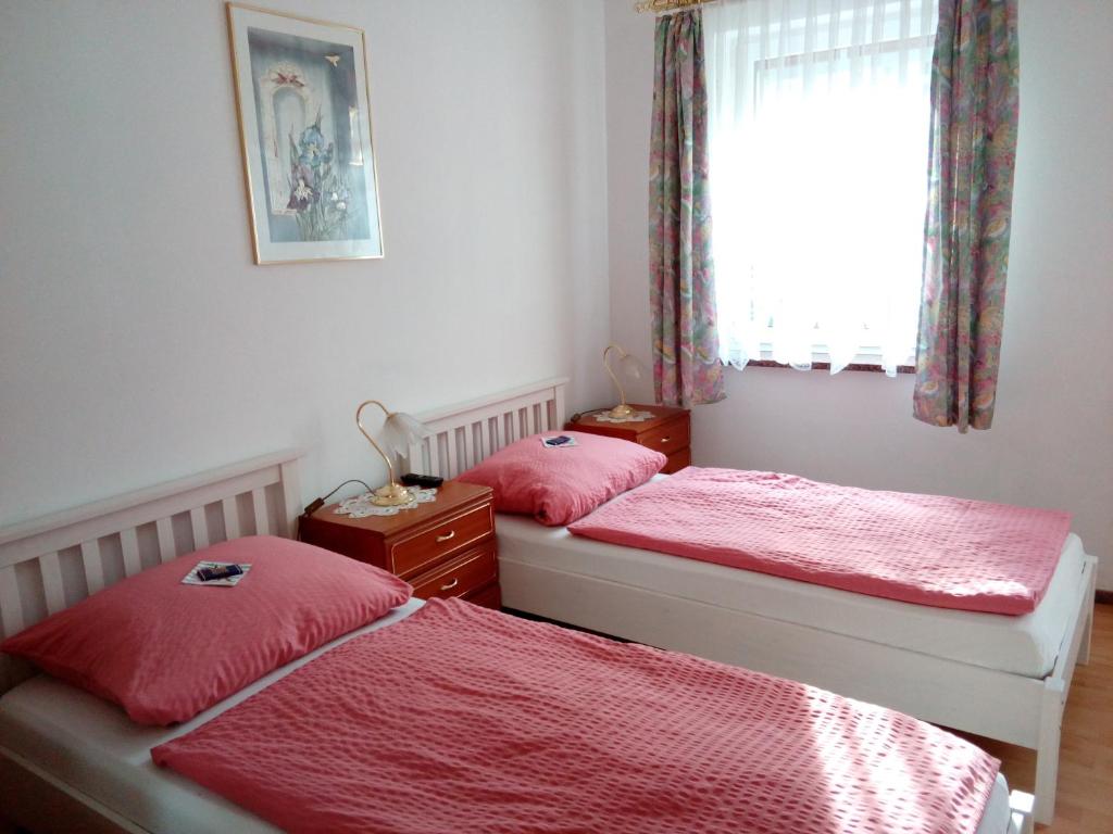 Duas camas num quarto com lençóis vermelhos e uma janela. em Pension Am Rosental Merseburg em Merseburg