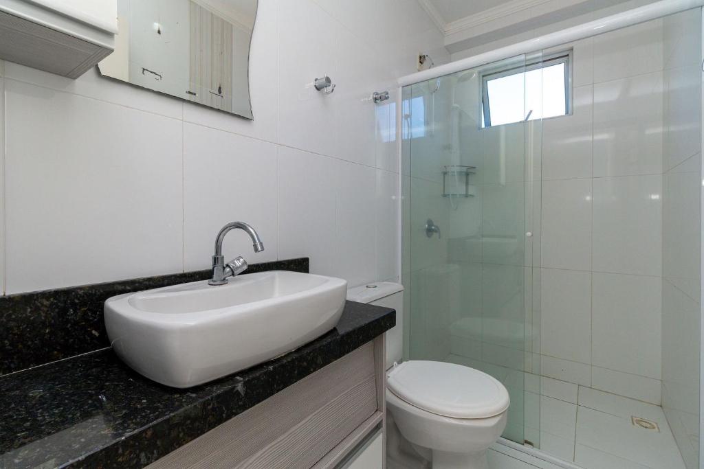 ein Bad mit einem Waschbecken, einem WC und einer Glasdusche in der Unterkunft Aluguel Apartamento 2 quartos vista mar Bombas/SC in Bombinhas