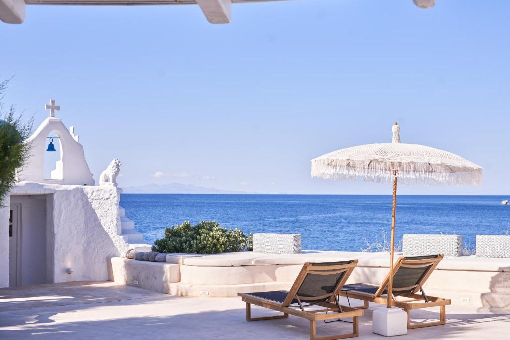 a patio with chairs and an umbrella and the ocean at Villa Santa Katerina - Sea View & Outdoor Hot Tub in Platis Yialos Mykonos